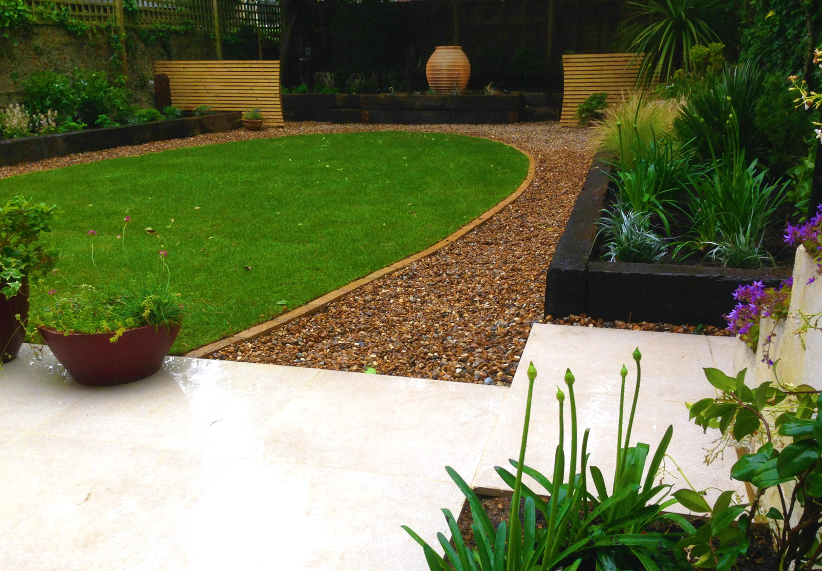Garden design in Hove, Sussex, with porcelain paving leading to oval lawn and large planting beds.