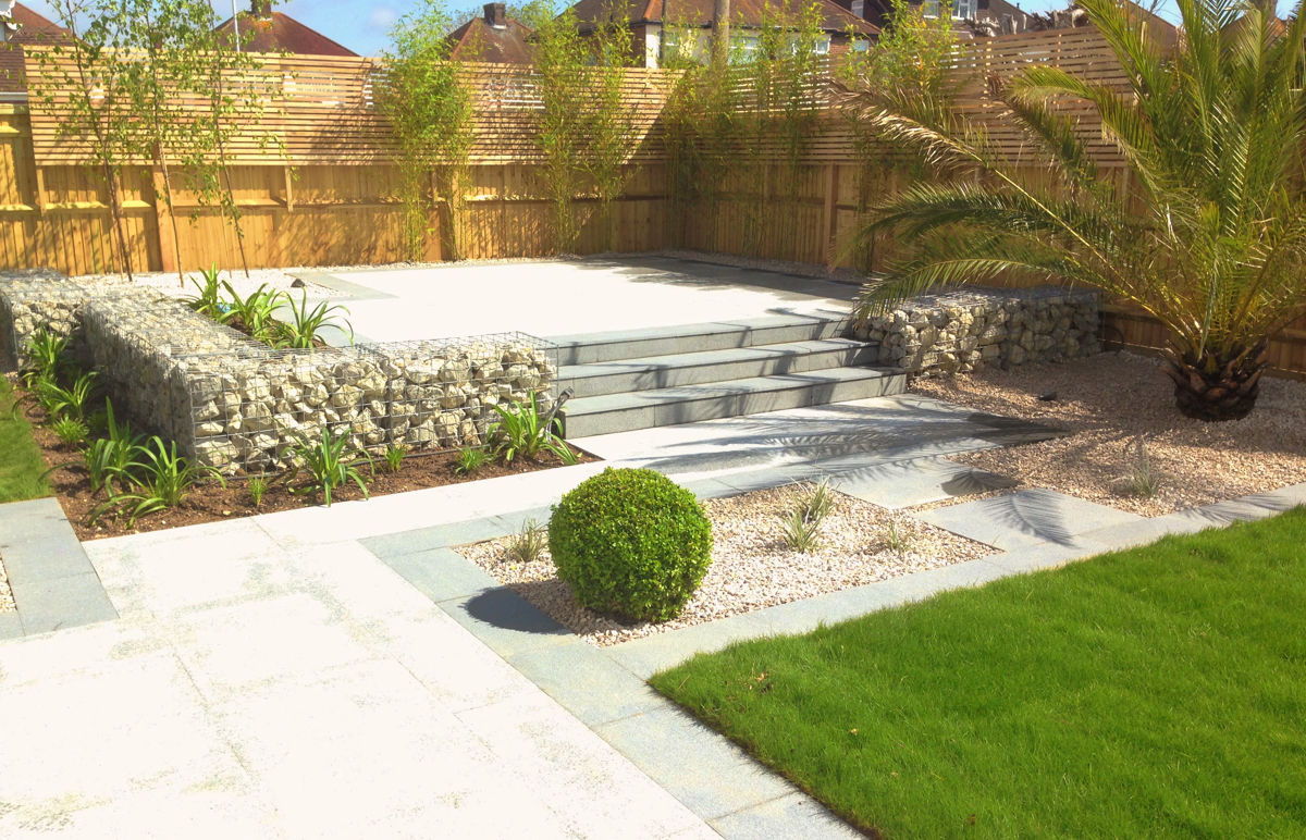 Large town garden in Worthing, West Sussex. Silver granite paving is edged with darker granite to highlights lawns and steps. Stone filled gabions create a level change up from two rectangular lawns